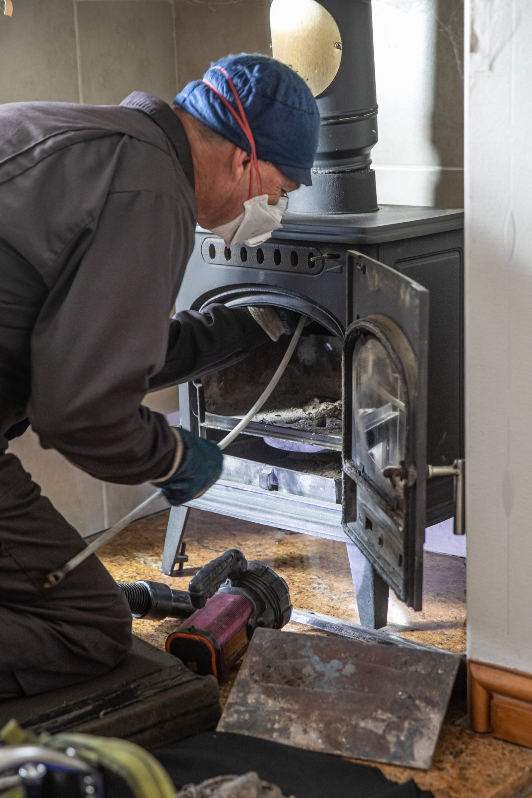 Chimney sweep cleaning a log mixed fuel burner with face covering and protective clothes